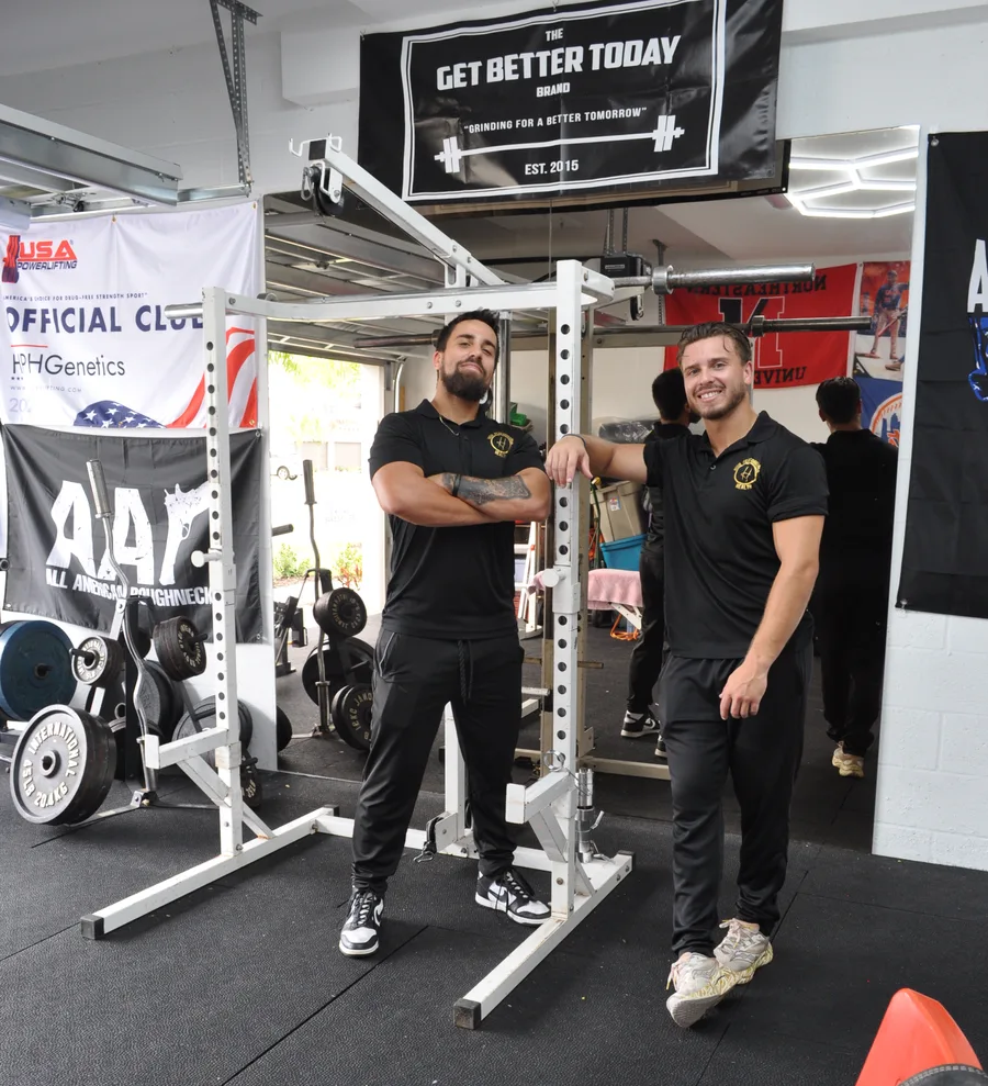 HPHGenetics co-founders Brian Ridzik (left, arms crossed) and Andy Ridzik (right, smiling) standing at a squat rack in the gym